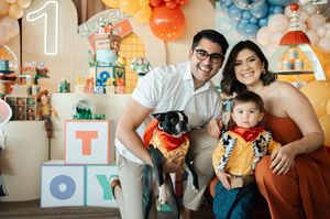 A family celebrates their child's first birthday party with their dog in a festive room decorated with balloons and toys.
