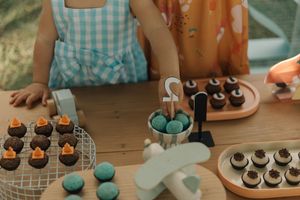 Several dessert platters display an assortment of chocolate cupcakes and turquoise macarons on white serving trays.