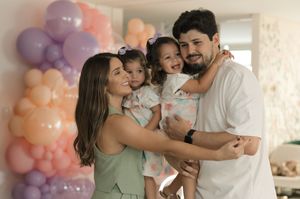 A happy family embracing and smiling at a celebration with pink and purple balloons in the background.