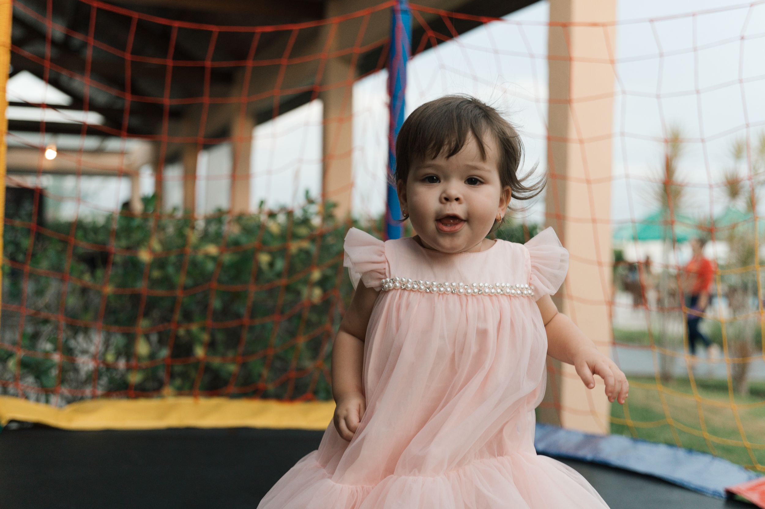 A collage of six photos showing a toddler in a pink dress playing and having fun outside.