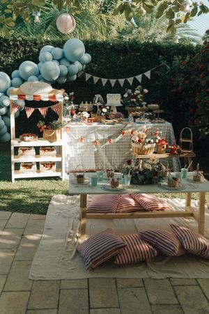 Outdoor garden party setup with blue balloons, striped cushions, and white furniture against lush greenery.