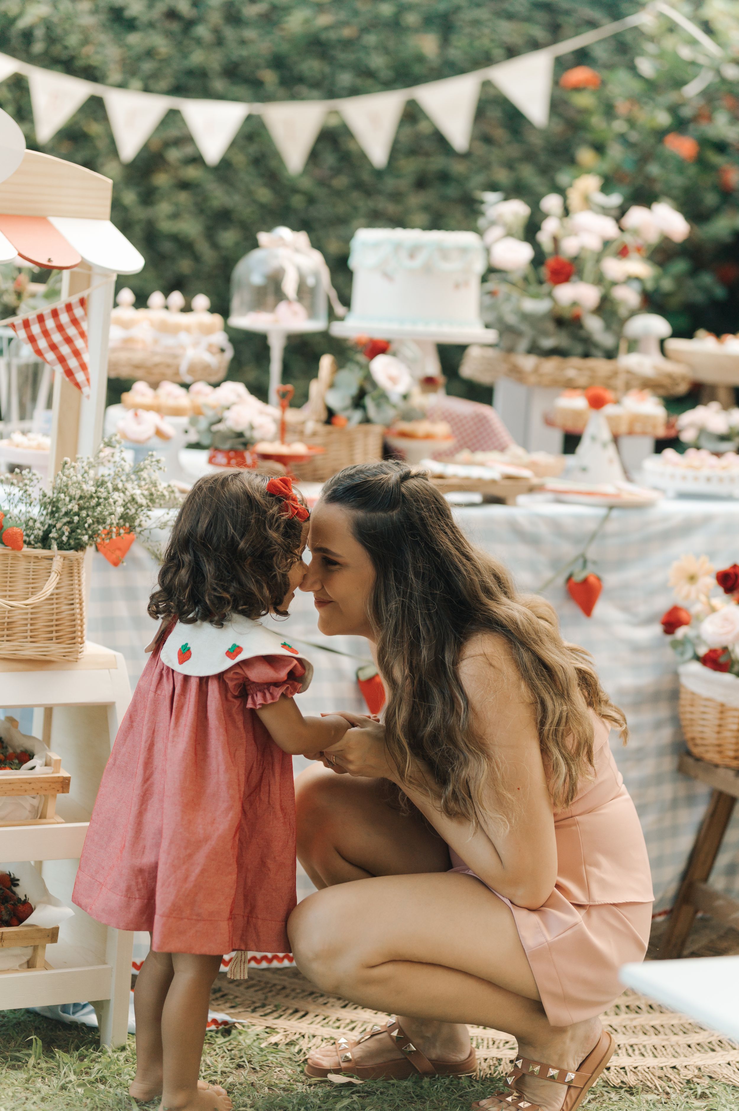 An outdoor party setup with pink decorations, bunting flags, and rustic table displays with treats for a celebration.