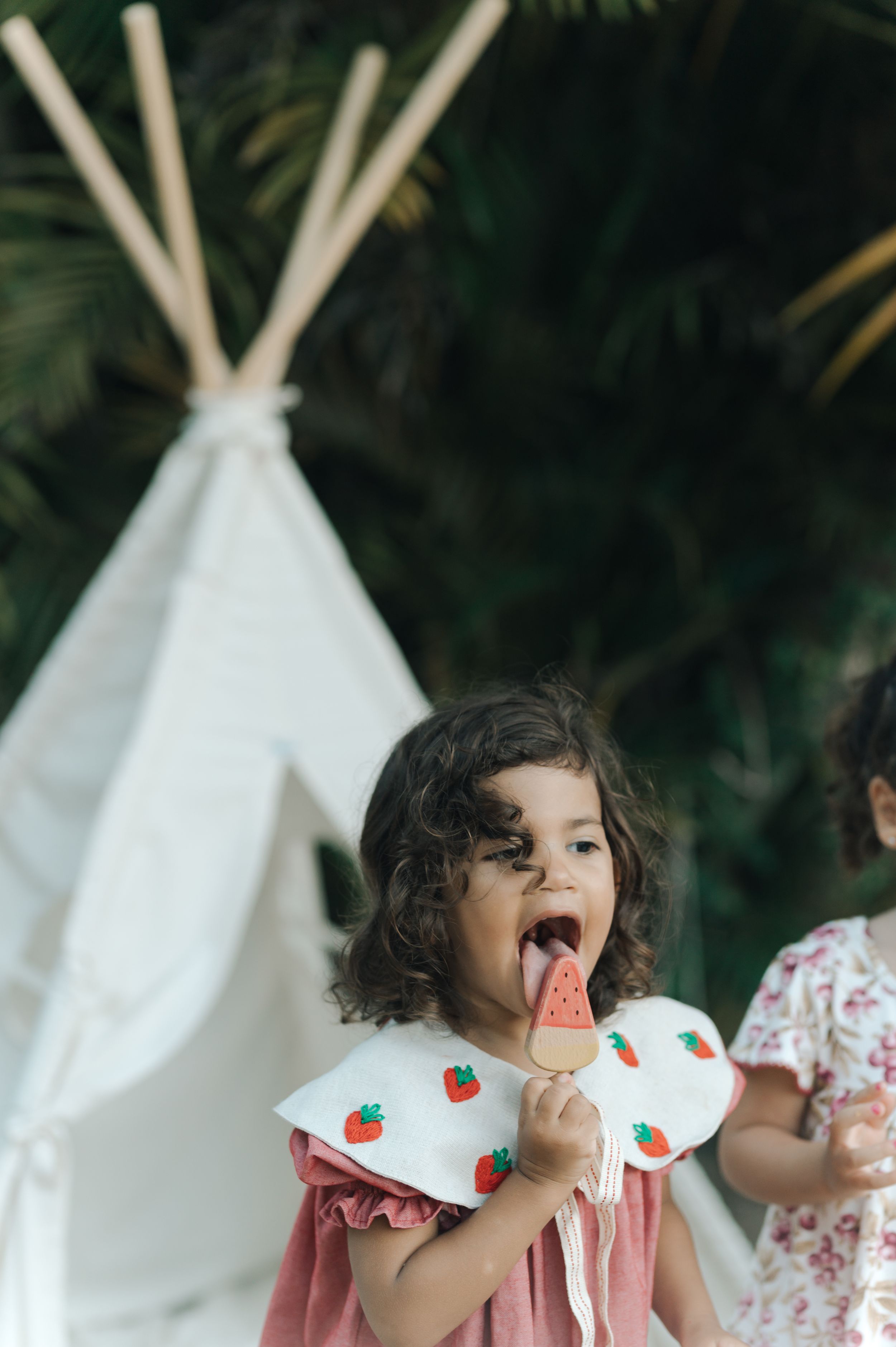 A child sits near a white tent having a snack in a whimsical garden setting.