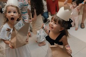 Two excited young children at a party showing expressions of joy and wonder on their faces, with one wearing a paper crown.