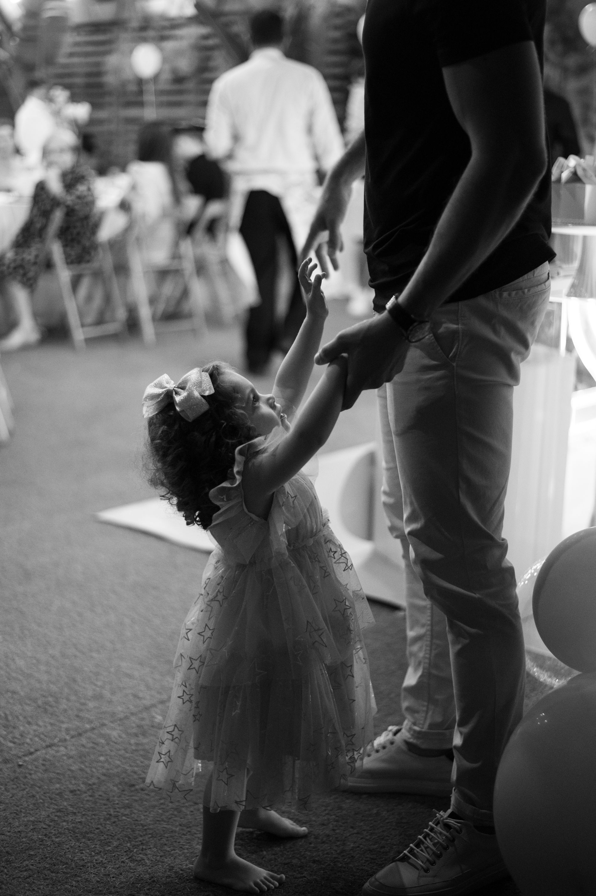 A black and white image of a small child in a tulle dress dancing at a party.