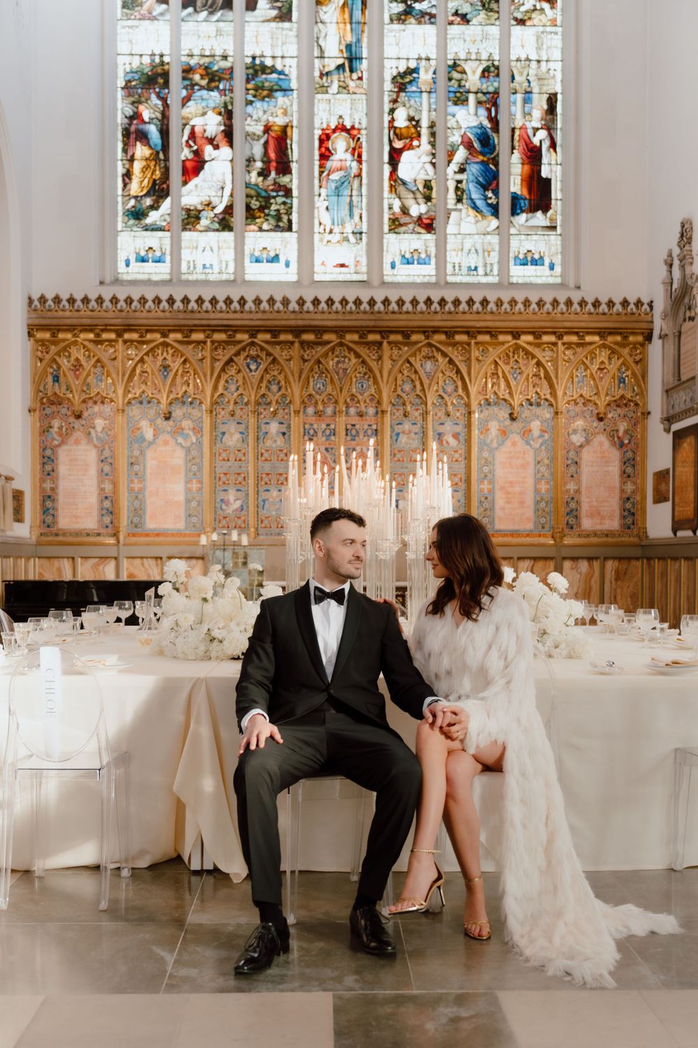 Elegant wedding venue interior with ornate gothic architecture, stained glass windows and decorated white reception tables.