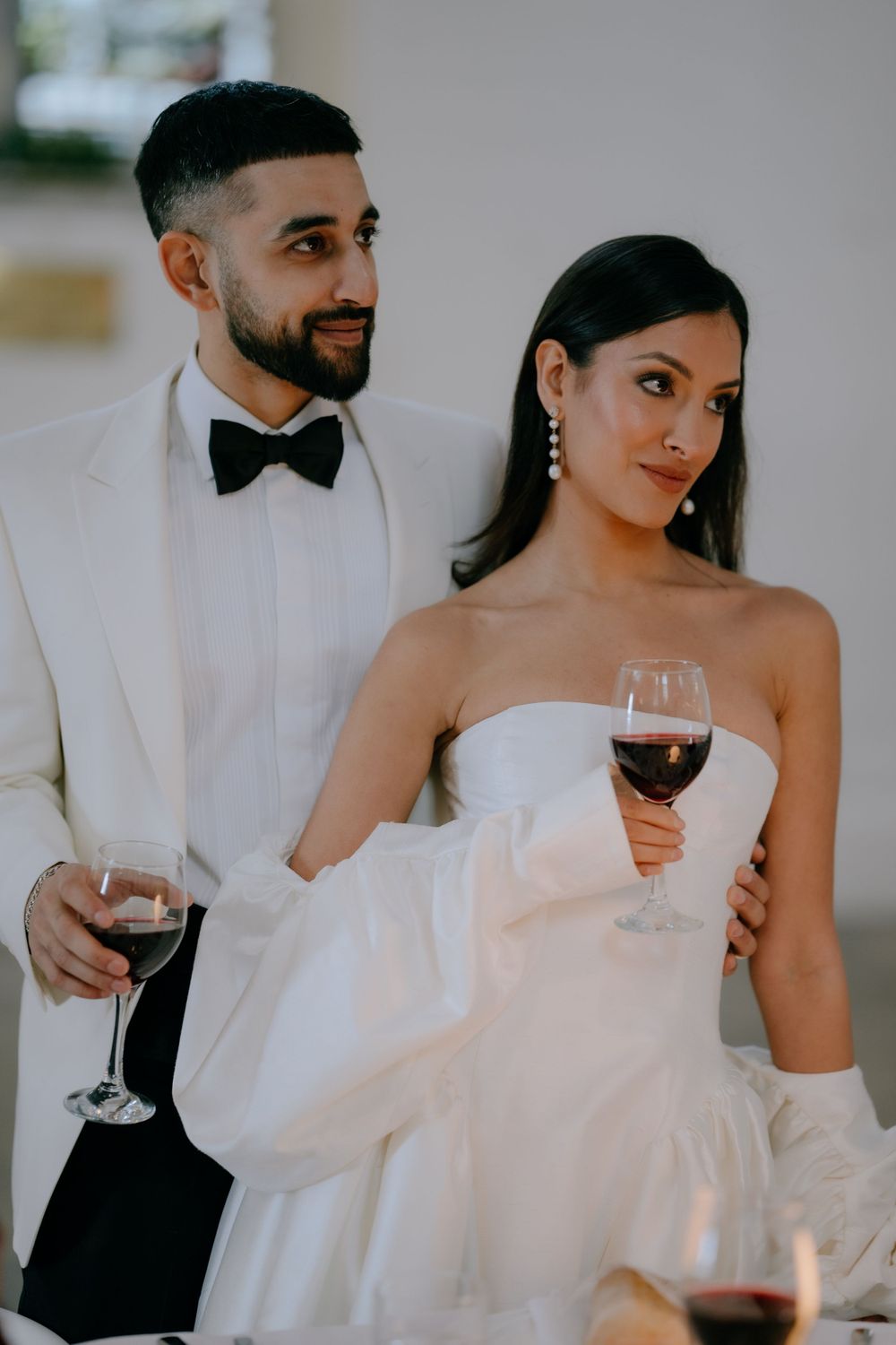Couple in formal wedding attire share wine during celebration.