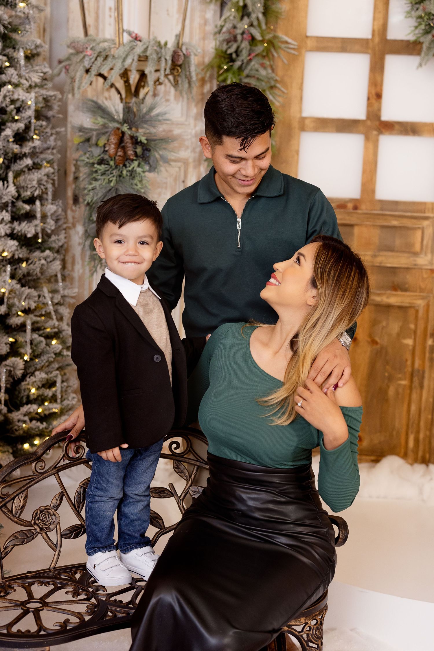 Family poses together in front of decorated Christmas tree in festive holiday studio setting.