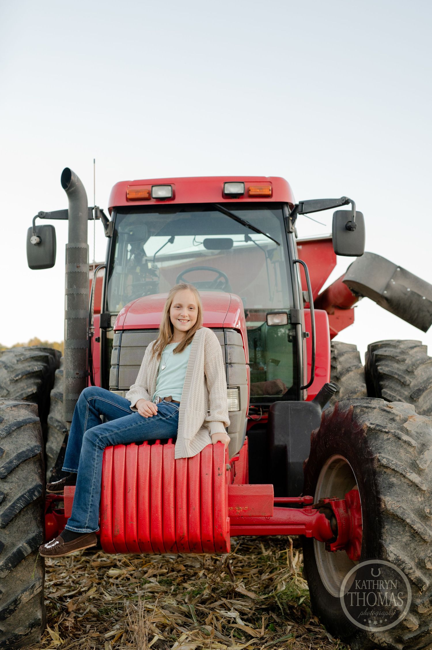 Student posing on a large red tractor in a farm field at sunset.