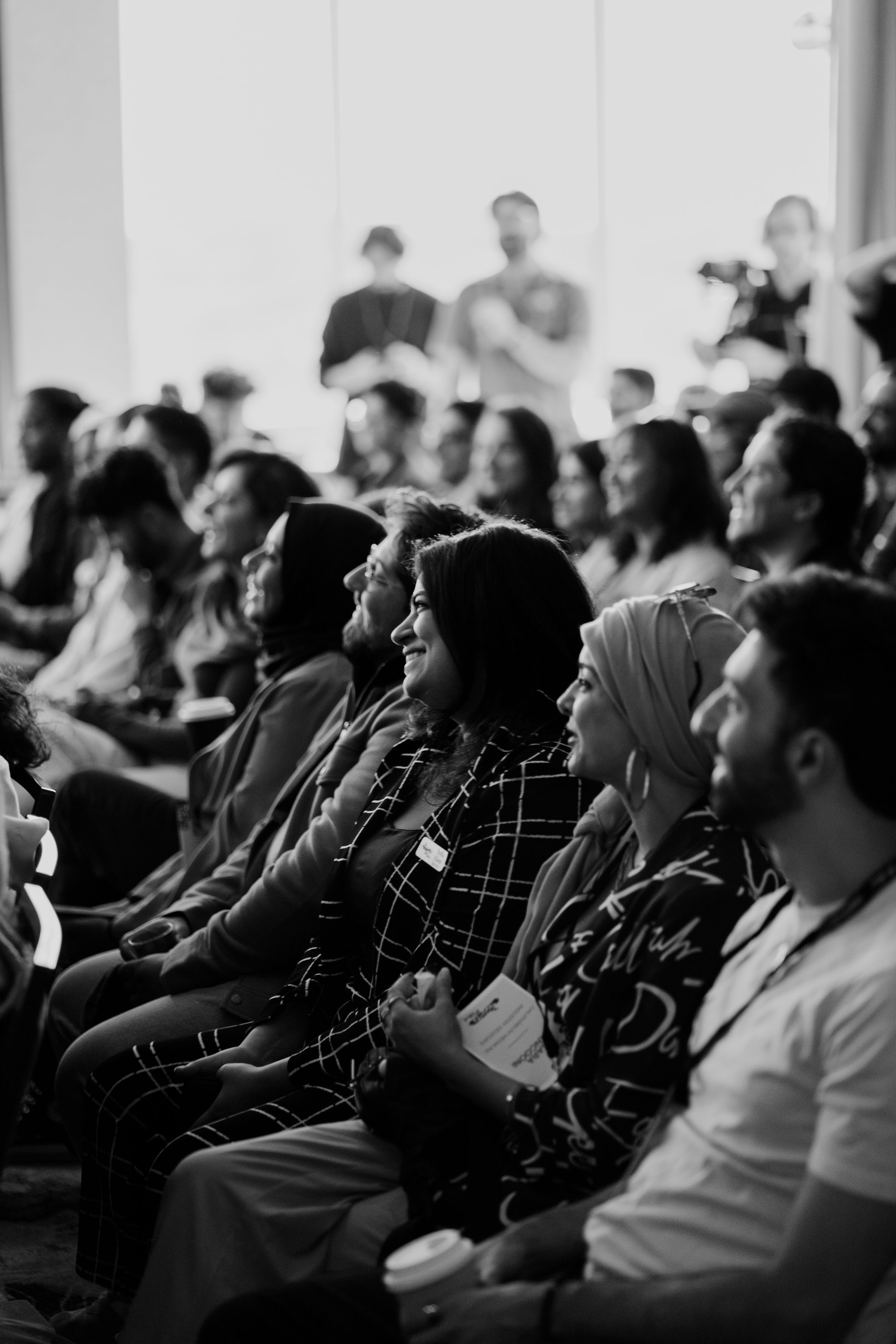 Black and white photo of diverse audience smiling at an indoor conference.