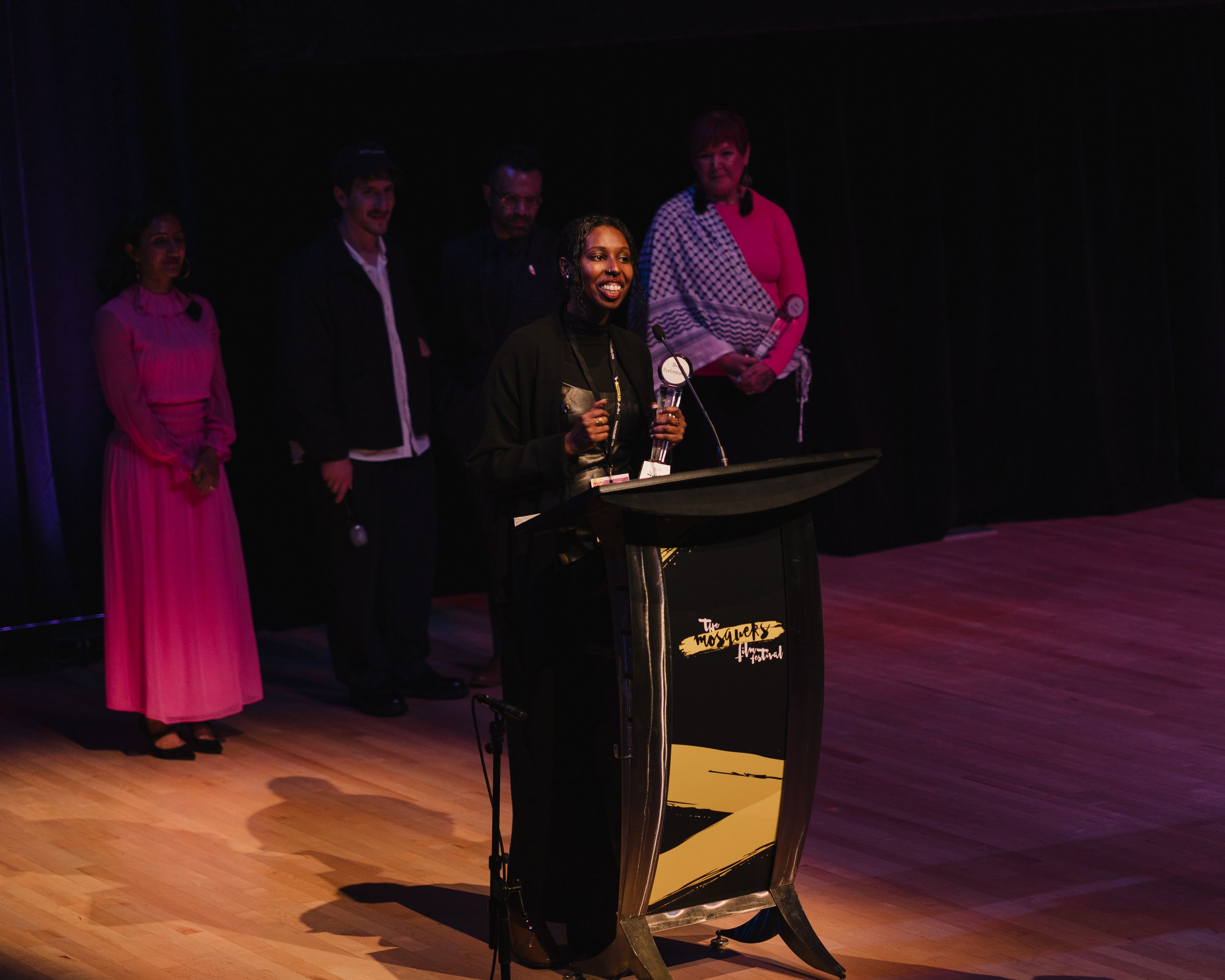 Person speaking at a podium on stage with group of people standing behind them.