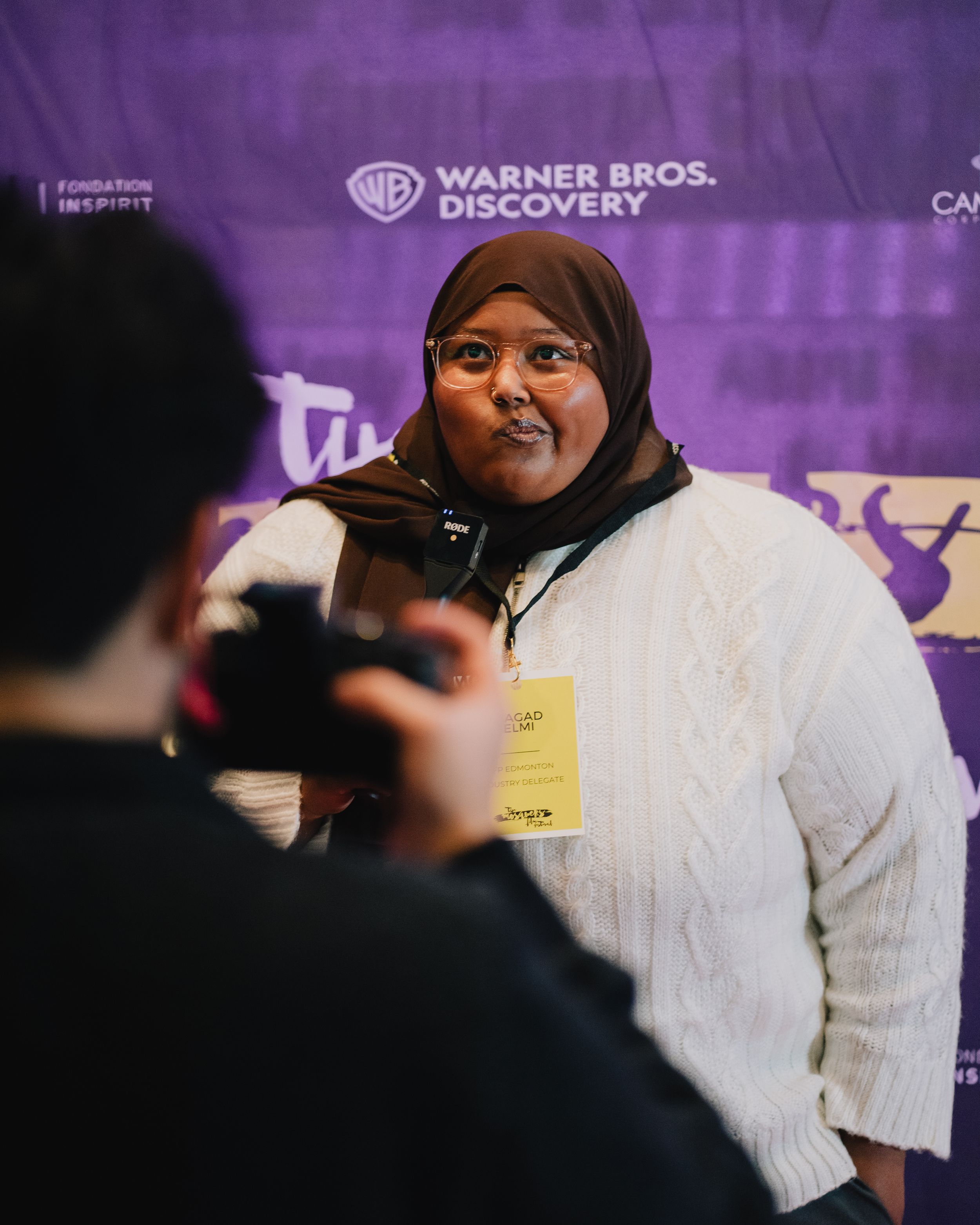 A woman in a hijab and white sweater poses for a photo at a Warner Bros. Discovery event.