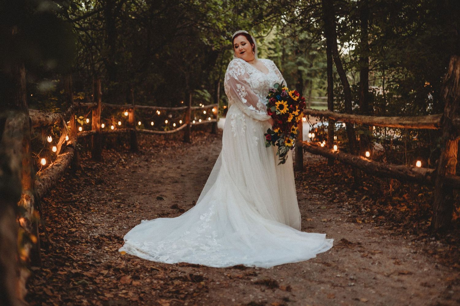 Wedding dress photographed against string lights in a wooded evening setting.