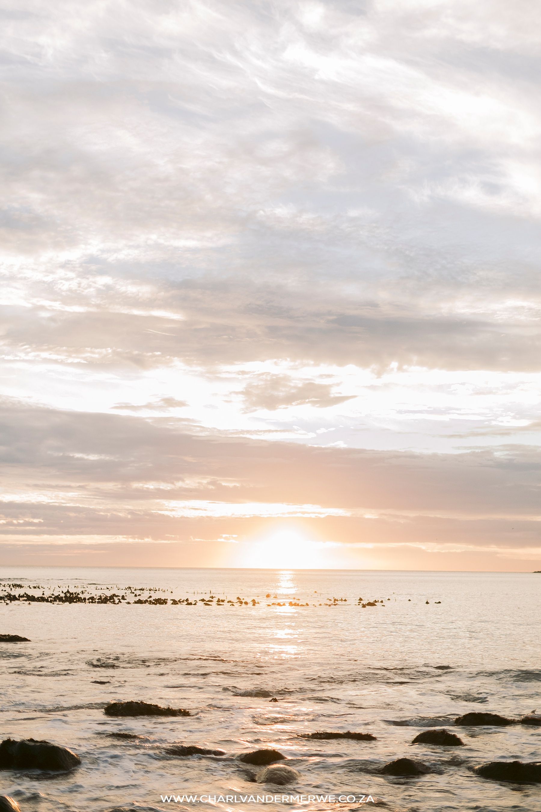 Golden sunset over calm ocean waters with rocky shoreline and dramatic cloudy sky.
