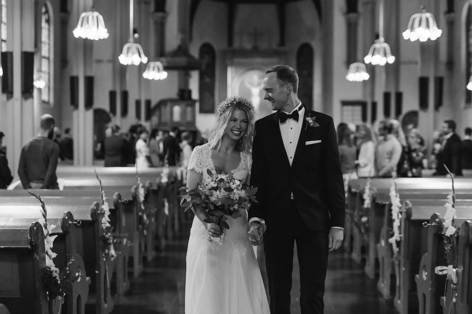Black and white photo of a bride and groom walking down the aisle of a church after their wedding ceremony.
