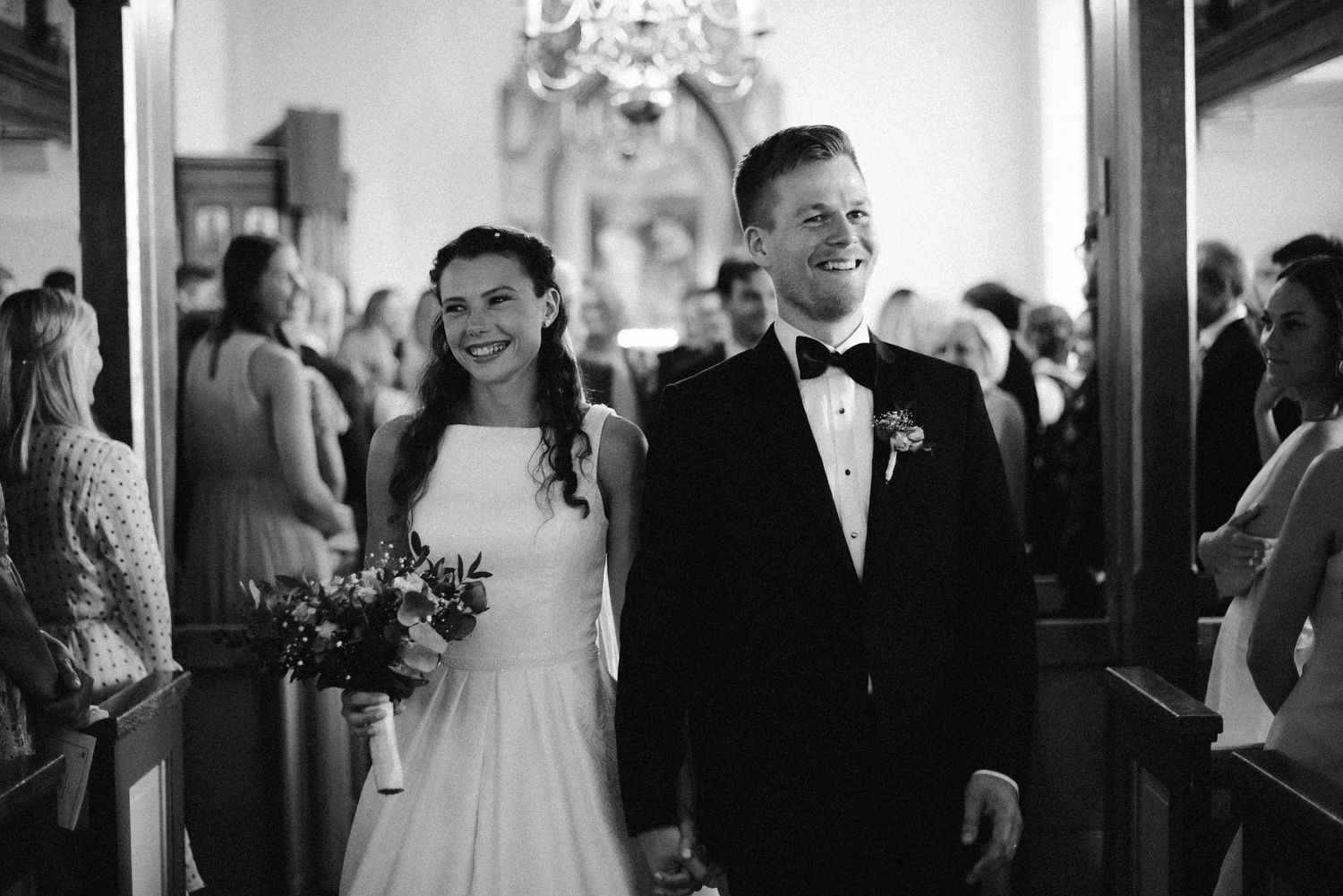 Black and white photo of a smiling bride and groom walking down the church aisle after their wedding ceremony.