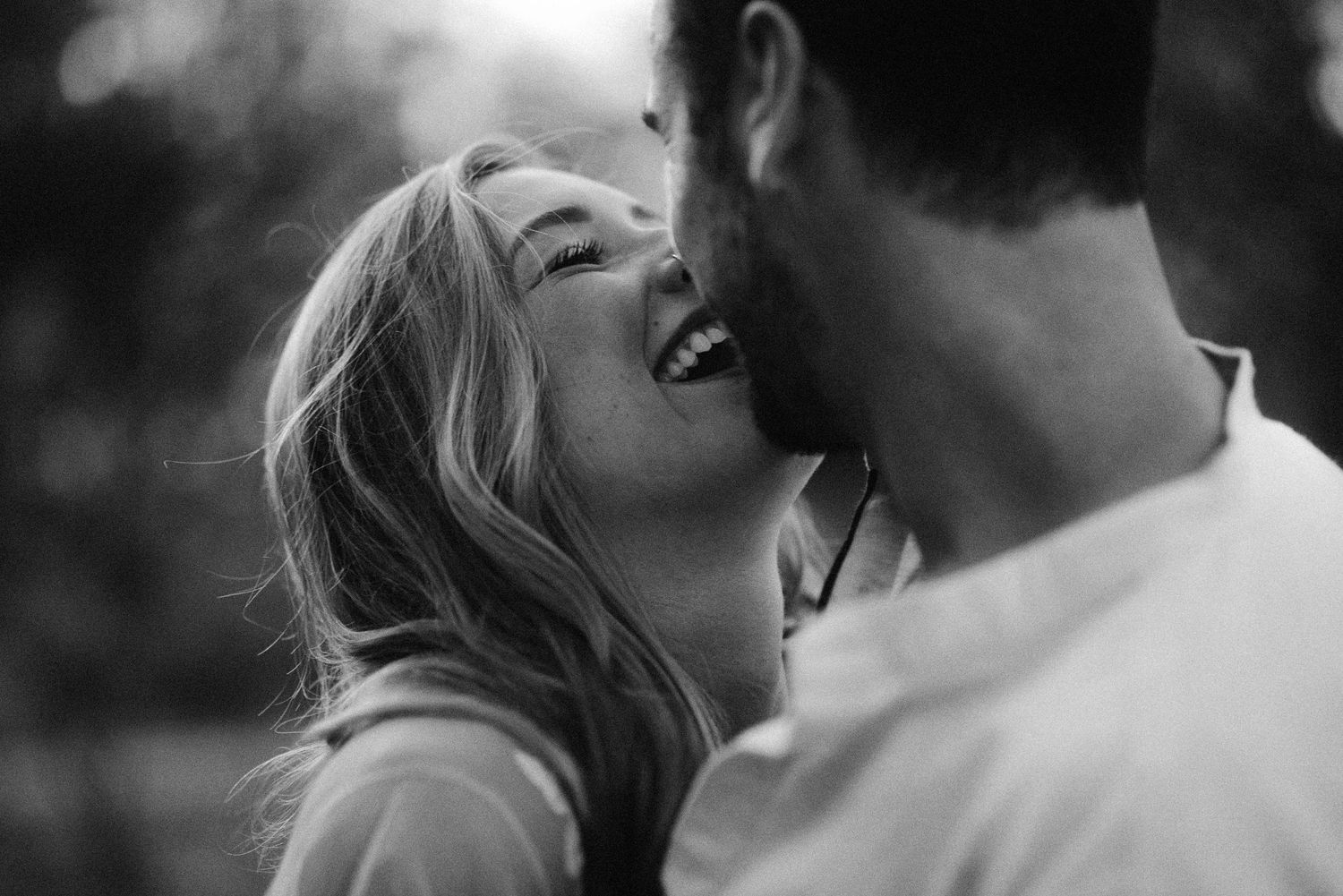 Black and white photo of a laughing couple sharing a joyful romantic moment outdoors.