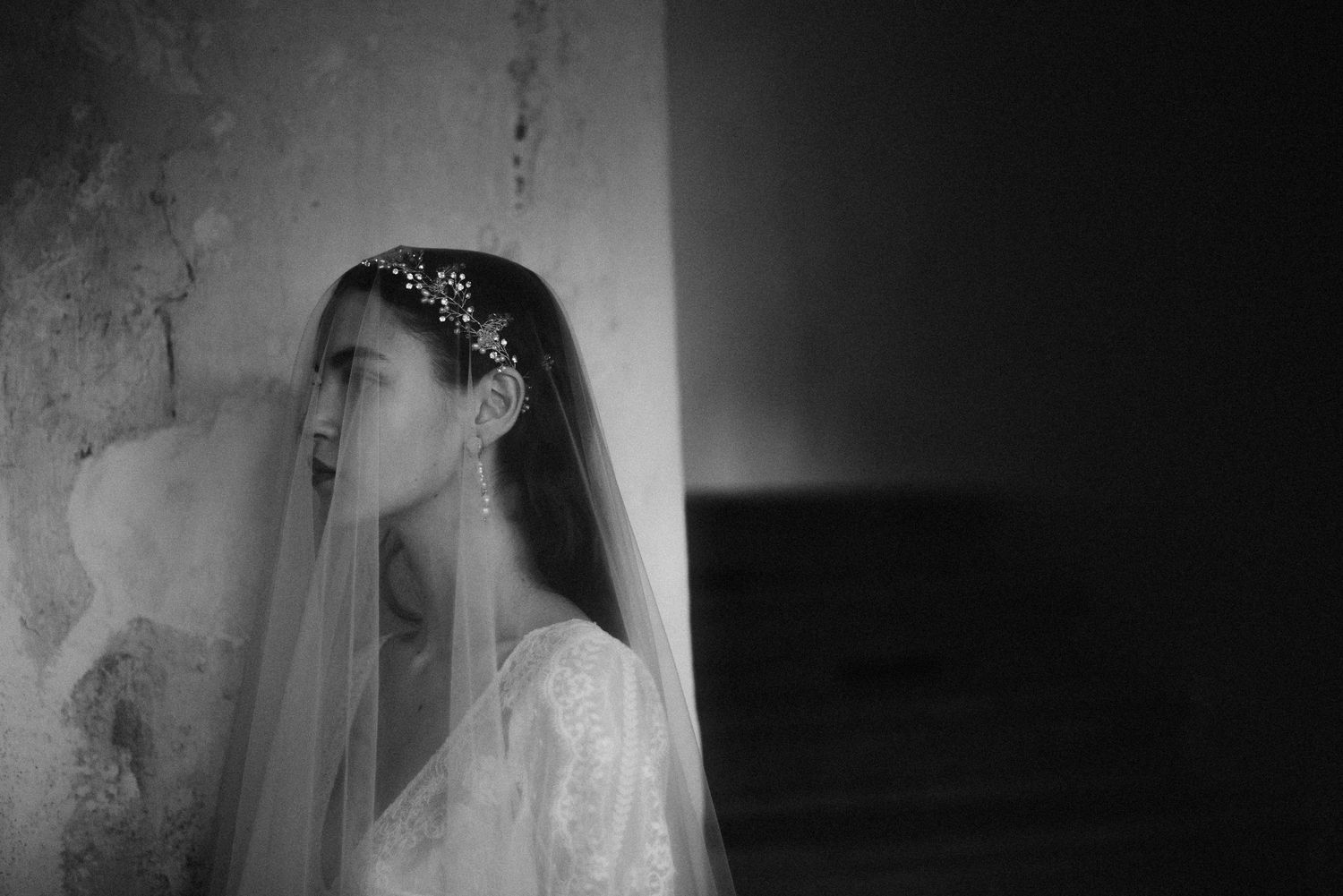 Dramatic black and white bridal portrait with vintage lace veil and crystal crown against textured wall.