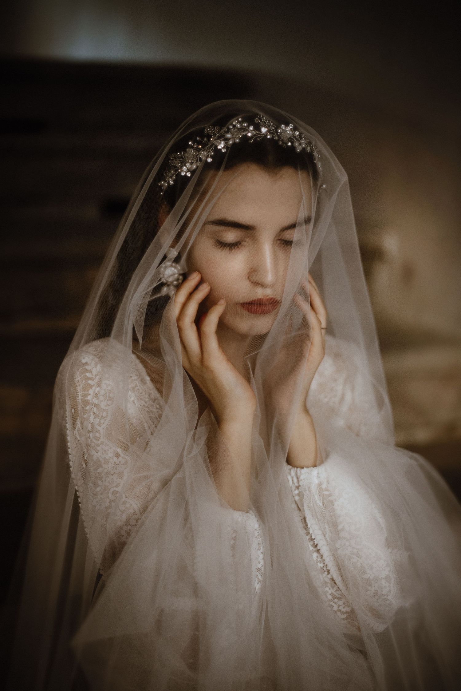 Ethereal moody bridal portrait with flowing lace veil and delicate crystal headpiece in warm sepia tones.