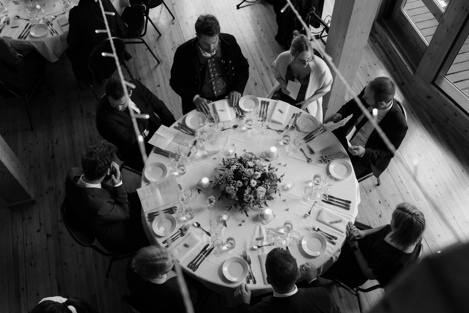 Aerial black and white photo of wedding guests gathered around a round table with floral centerpiece.