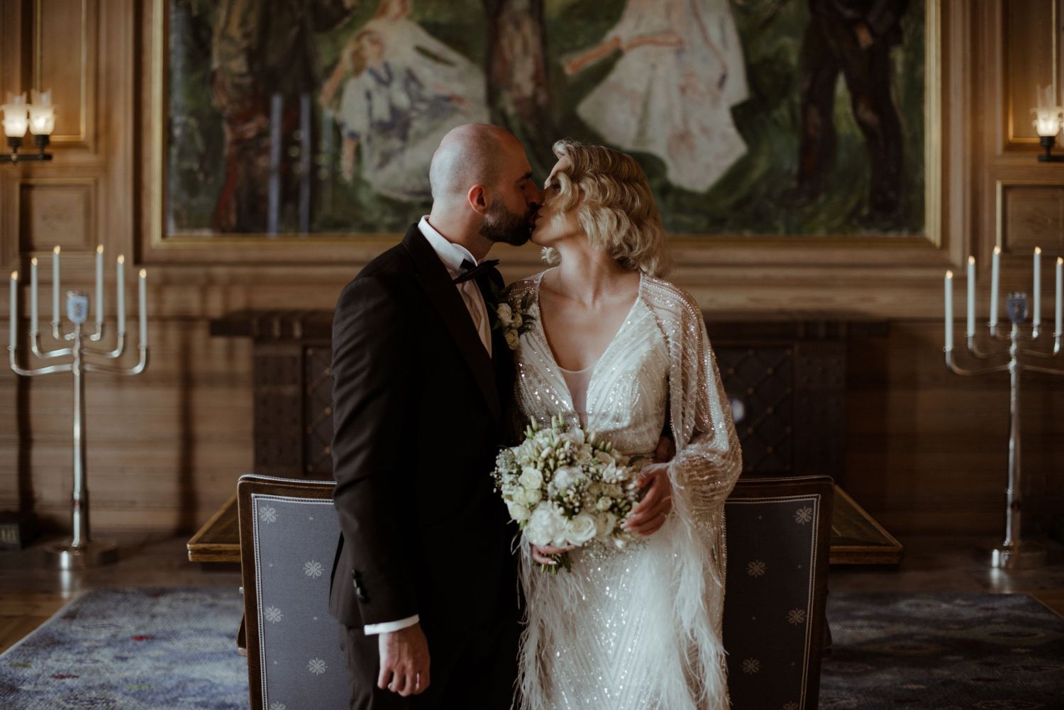 Bride and groom share a romantic moment in an elegant hall, bride holding a white bouquet in a lace gown.