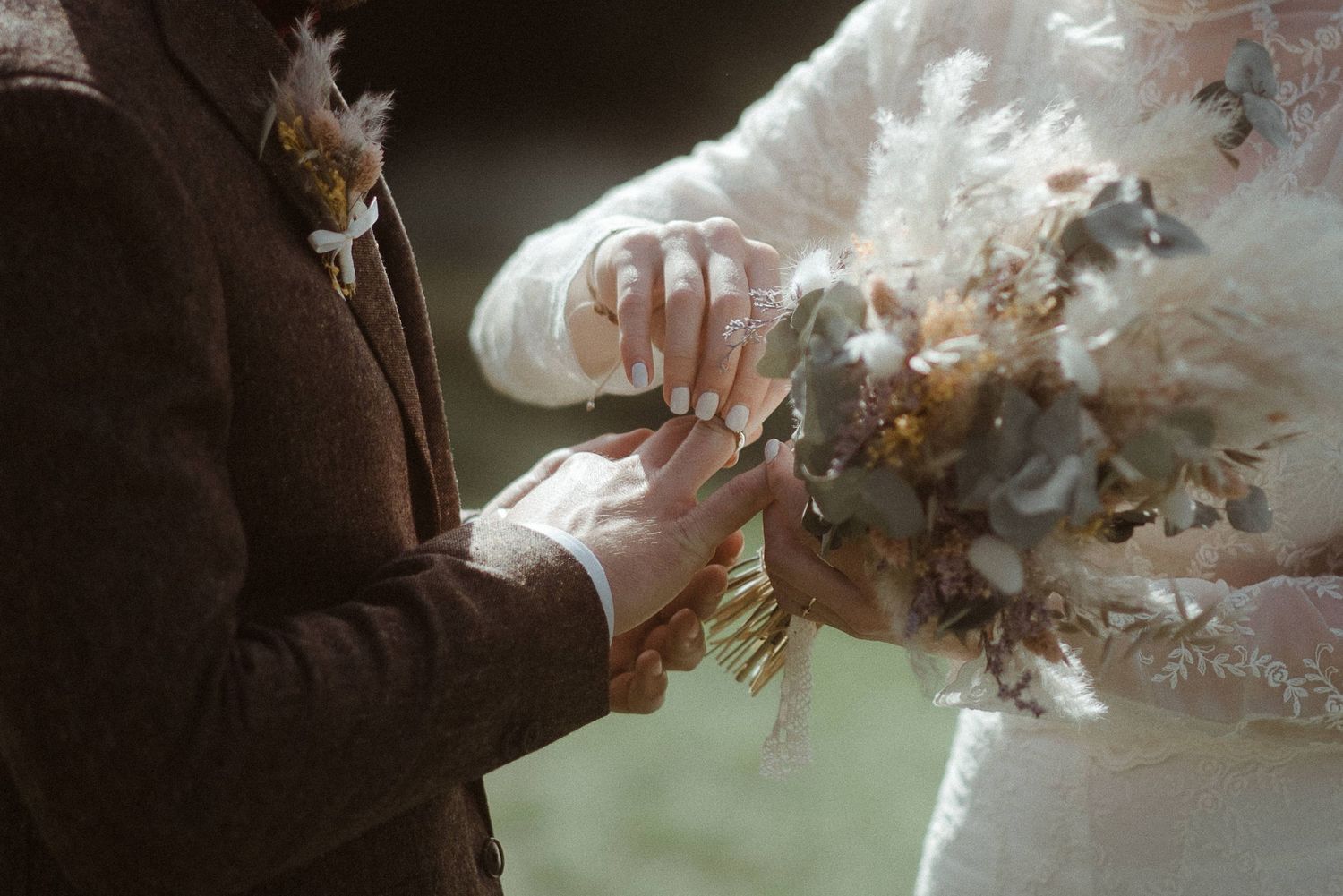 Bride and groom exchanging rings during wedding ceremony, bride holding a rustic dried flower bouquet.