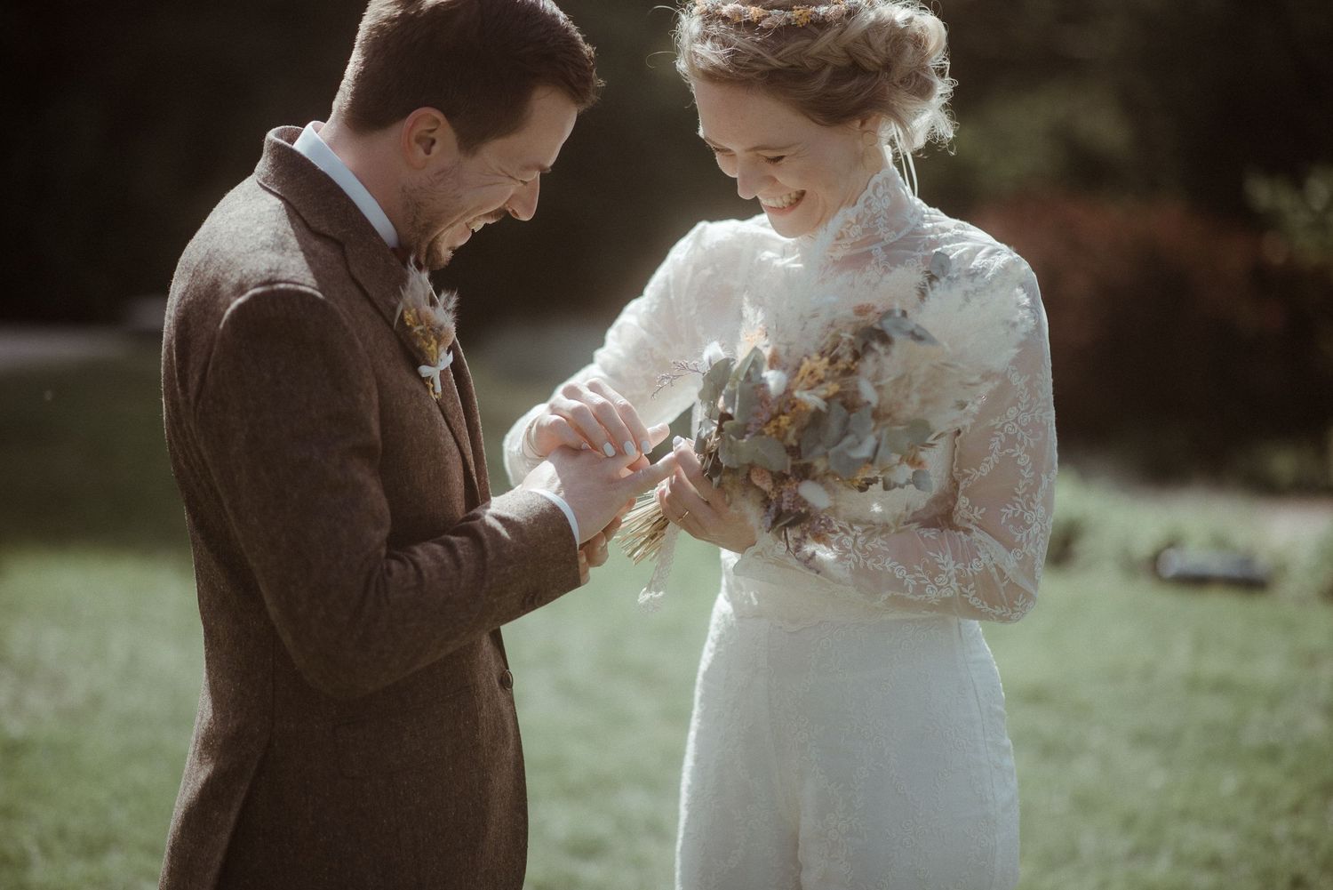 Bride and groom exchanging rings outdoors during autumn wedding ceremony, bride holding dried flower bouquet.