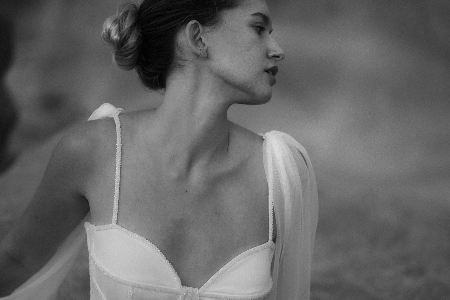 Black and white bridal portrait of elegant woman in spaghetti strap wedding gown with flowing veil detail.