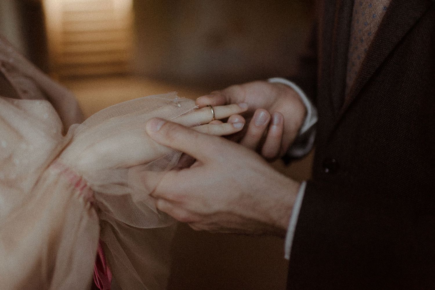 Close-up of a groom placing a gold wedding ring on the bride's finger during a wedding ceremony.