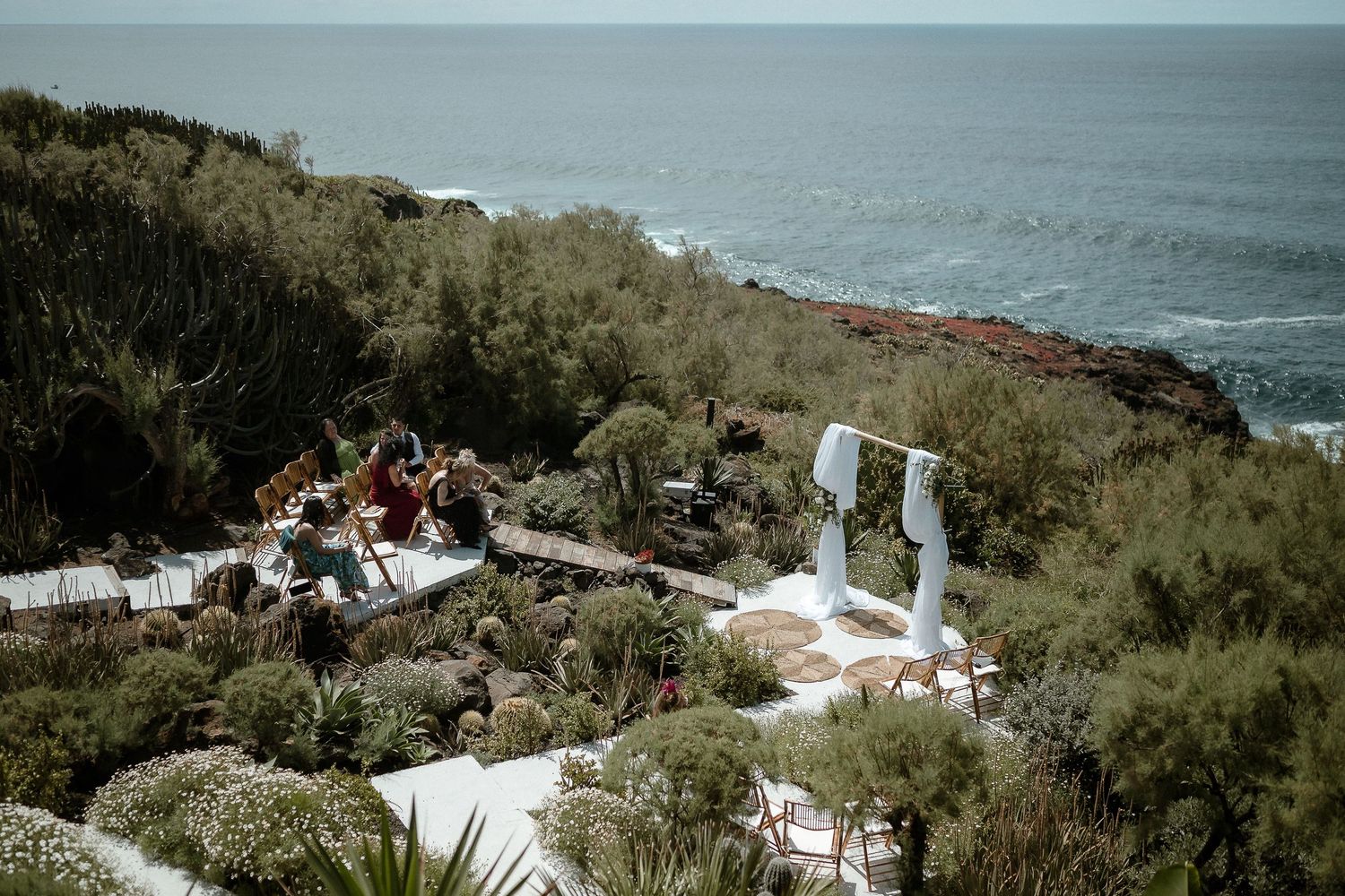 Aerial view of a coastal cliffside wedding venue surrounded by lush greenery overlooking the ocean.