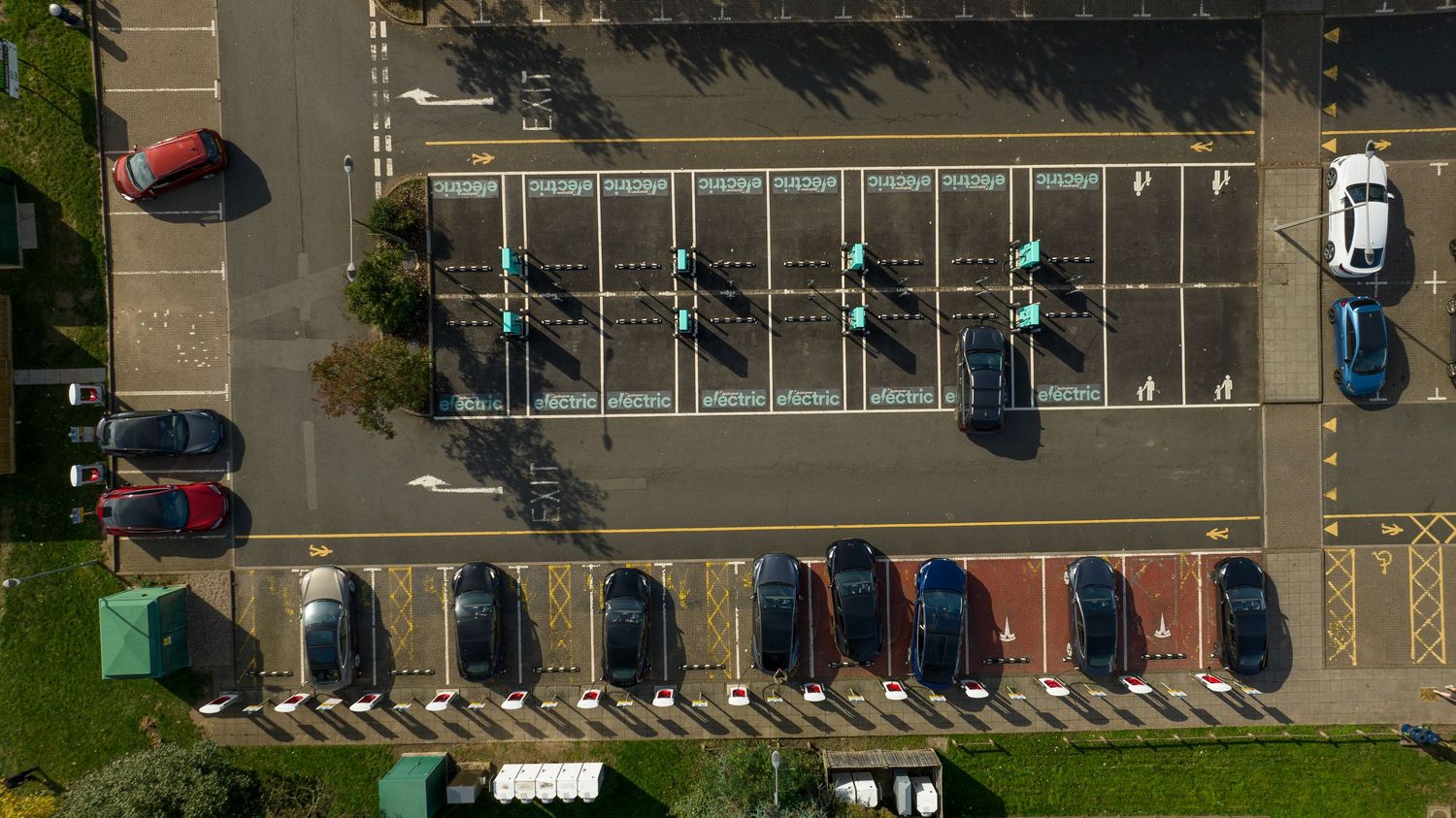 Aerial view of a parking lot with cars neatly arranged in rows and green grass visible on the side.