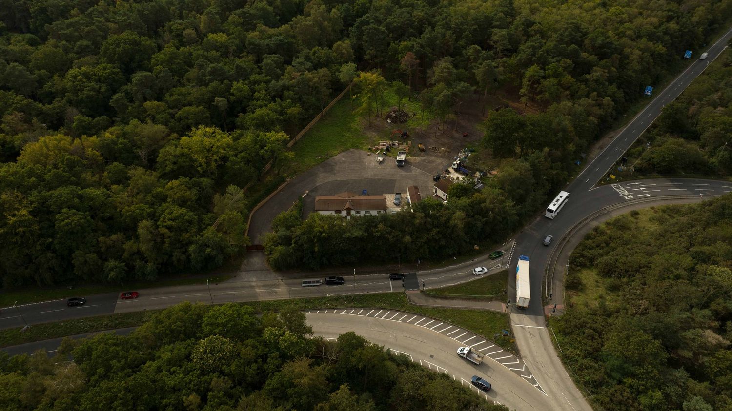 Aerial view of a forested highway intersection with curved entrance ramps and access roads surrounded by dense trees.