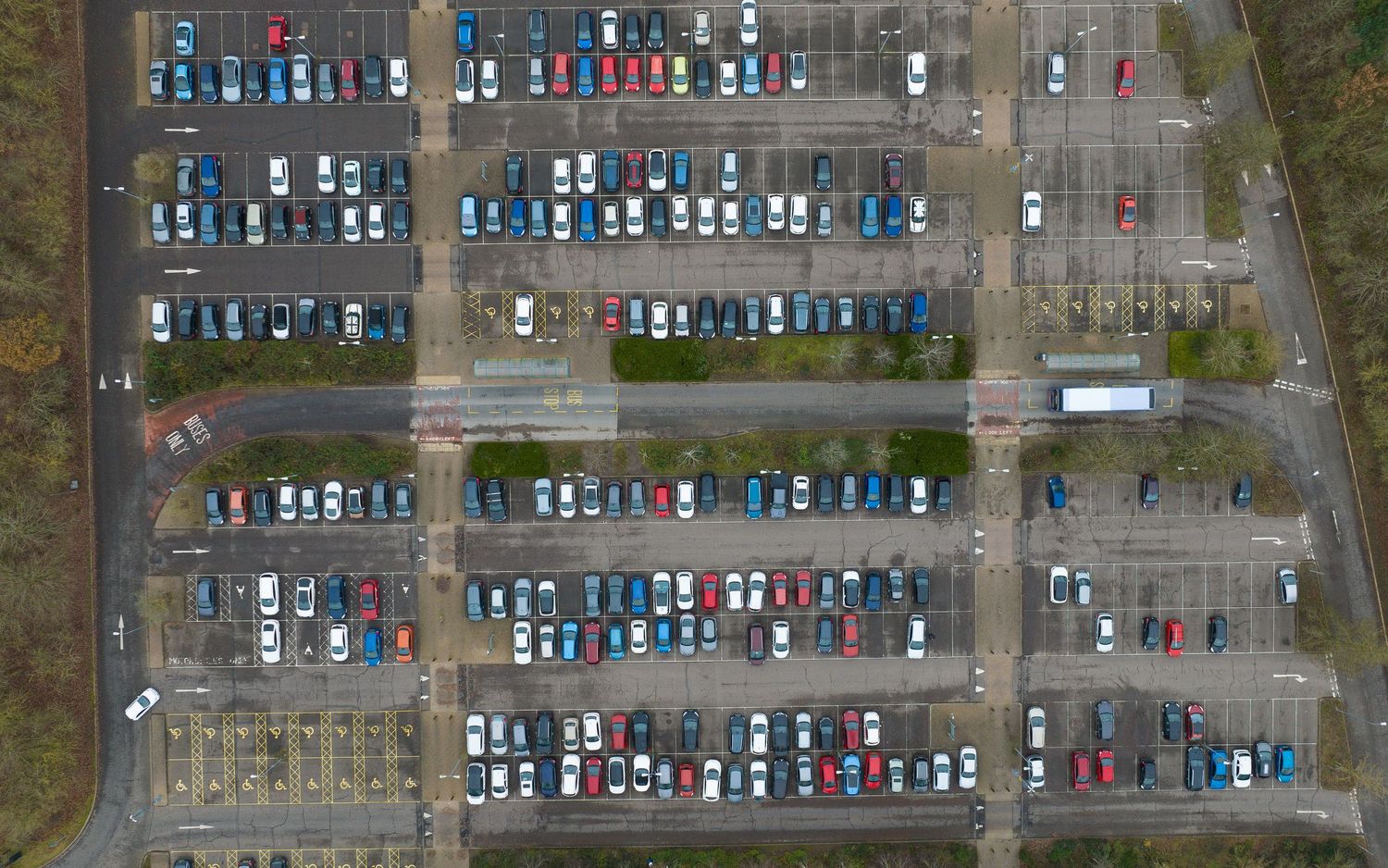 Aerial view of parked cars in multiple rows at a large outdoor parking lot surrounded by trees.