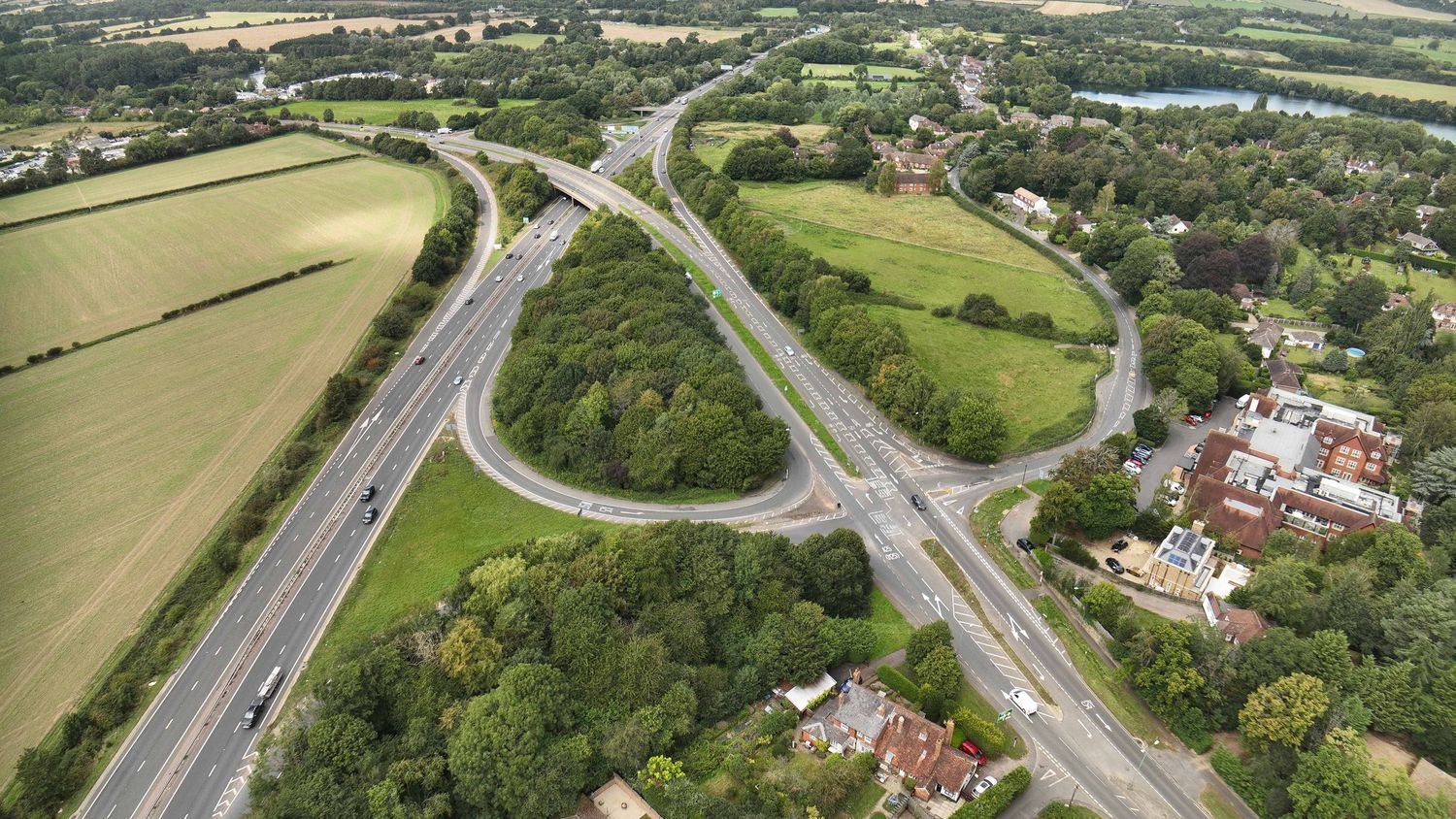Aerial view of a highway interchange with cloverleaf ramps surrounded by green fields and countryside in England.