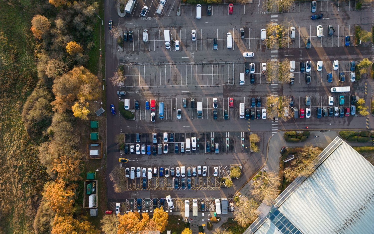 Aerial view of parked cars in a parking lot surrounded by autumn trees with golden foliage.