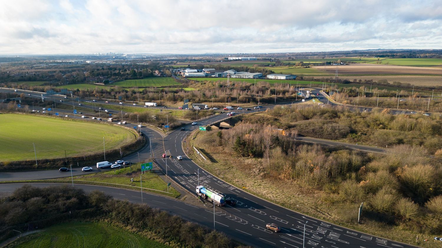 Panoramic aerial view of a green countryside landscape with winding roads, farmland and scattered buildings.