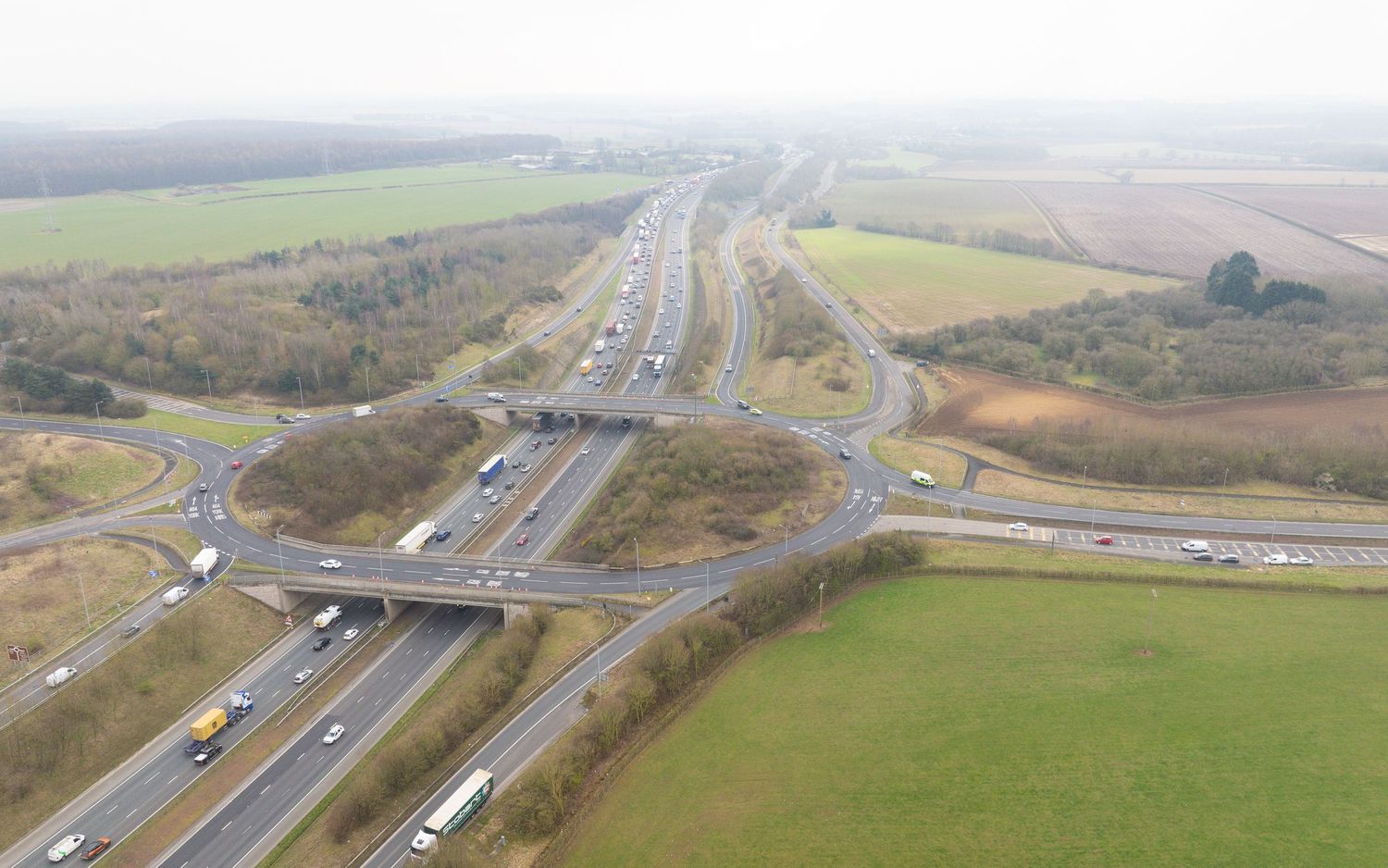 Aerial view of rural highway interchange with connecting ramps and green agricultural fields in the countryside.