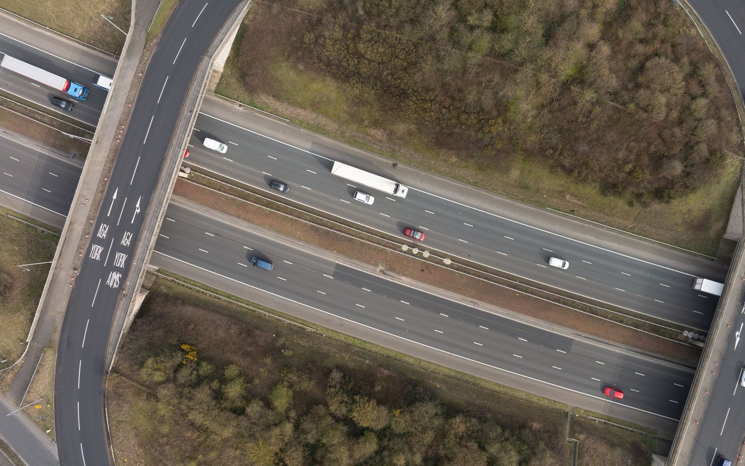 Aerial view of highway intersection with vehicles traveling beneath an overpass bridge on a clear day.