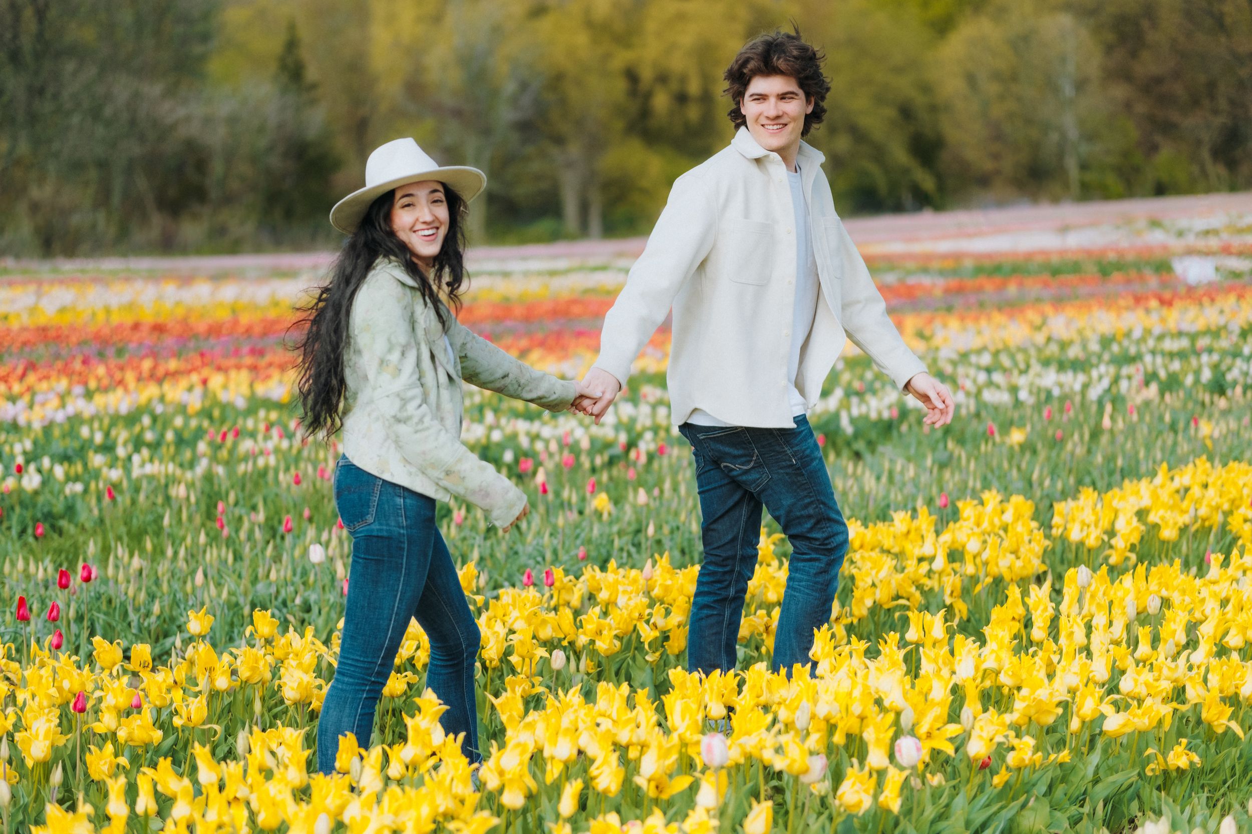 Couple holding hands while walking through field of yellow daffodils.
