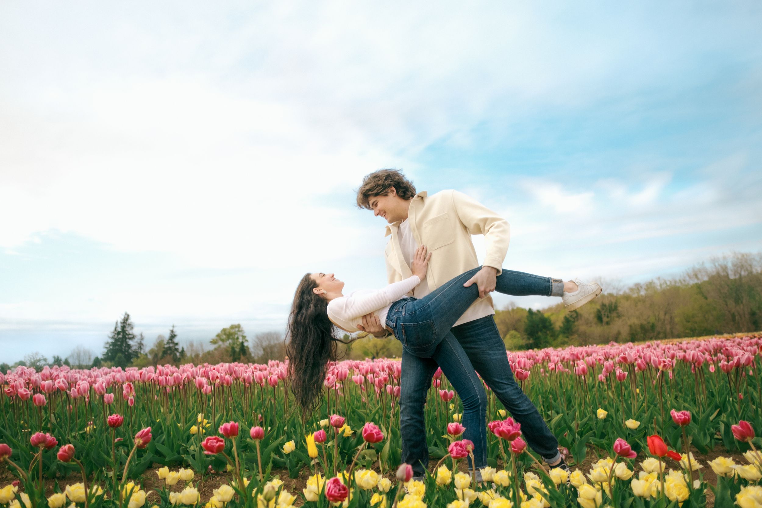 Playful couple dipping pose in colorful tulip field under blue sky.