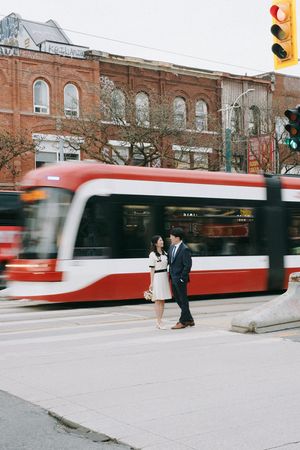 A couple shares a moment on a city street as a red streetcar passes by historic buildings.
