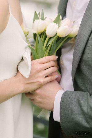 Hands hold a bouquet of white tulips during an intimate moment.