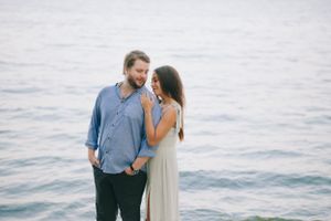 A romantic couple stands together by the ocean at sunset enjoying an intimate moment.
