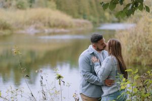 A romantic couple shares an intimate moment by a serene lake surrounded by autumn foliage.