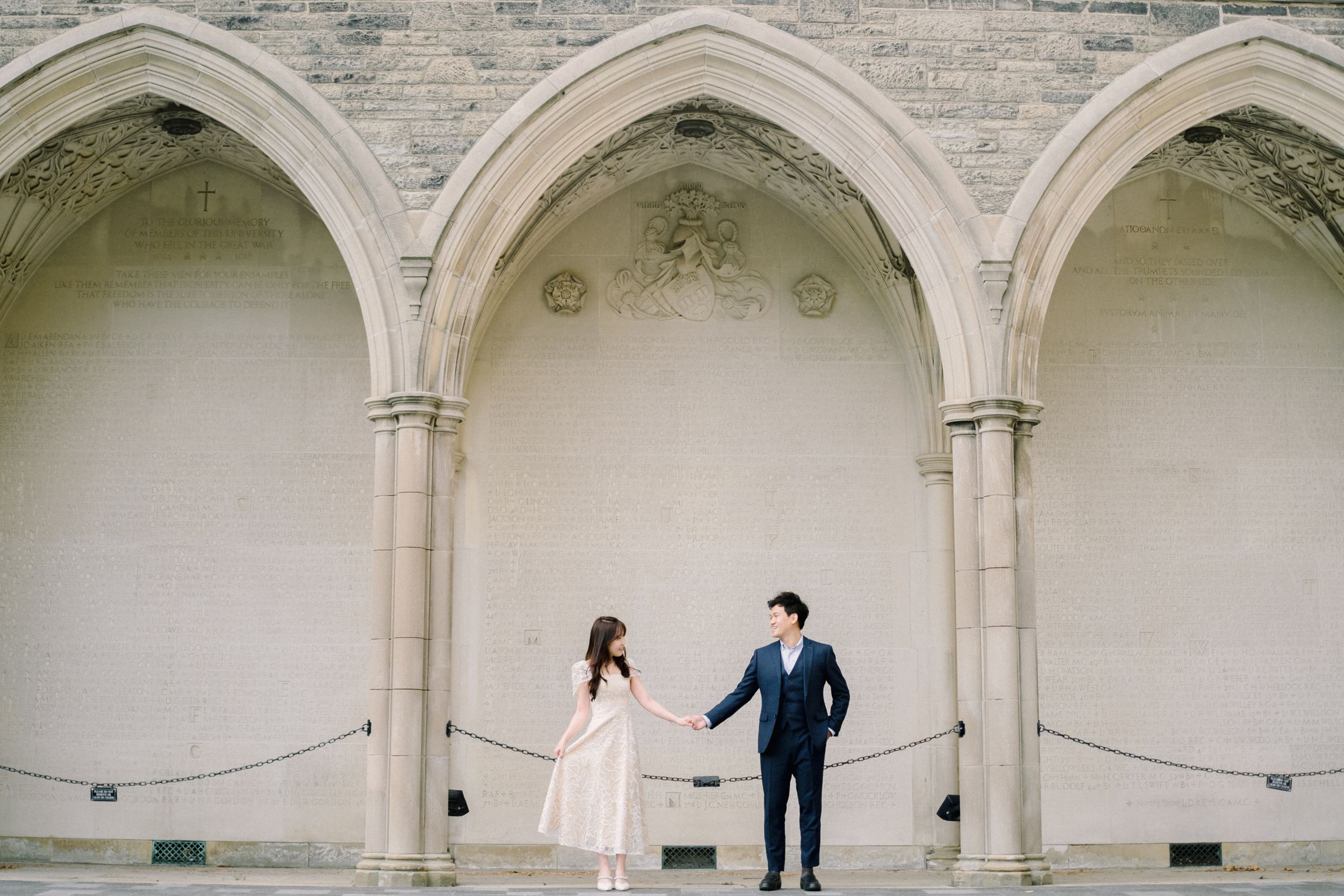 A romantic couple shares a tender moment under the grand stone arches of a historic building.