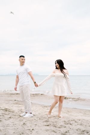 A couple enjoys a playful moment on a sandy beach near the ocean.