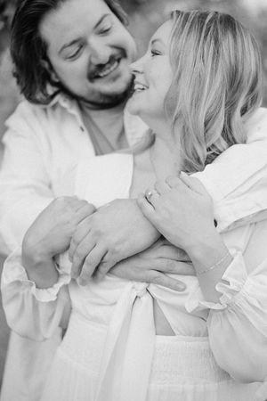 A romantic black and white photo of a couple embracing and laughing while wearing white clothing.