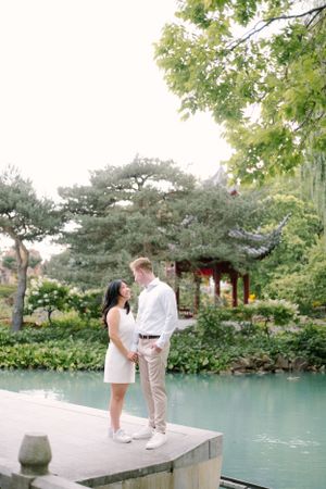 A couple poses together on a stone platform overlooking a serene garden pond with pagoda in background.