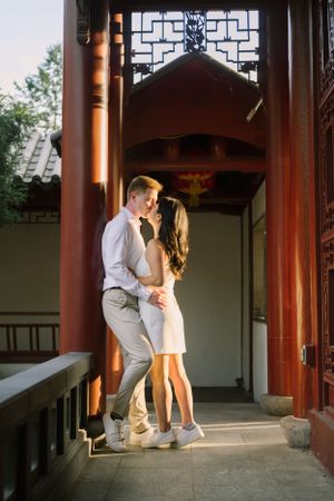 A couple shares an intimate moment in a traditional Asian architectural setting with ornate red pillars.