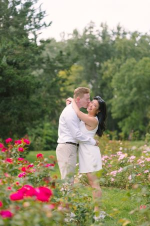A couple embraces in a vibrant garden with blooming red roses and green foliage.